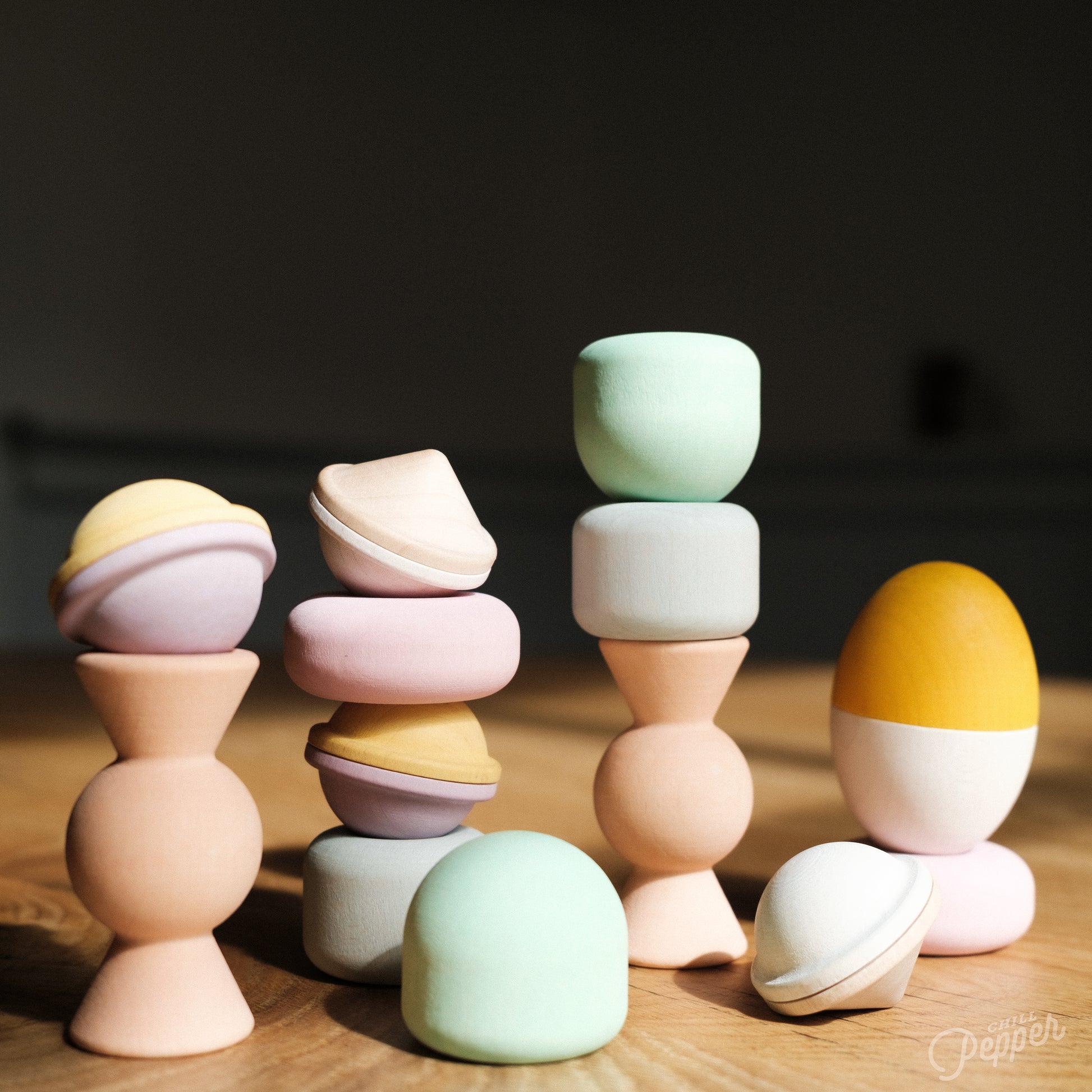 Wooden Chill Pepper Treats stacking and spinning game for ages 3 and up, made from eco-friendly maple wood and non-toxic, water-based paints. The set includes a variety of pastel-colored candy-shaped pieces and a unique Magic Egg for open-ended play.