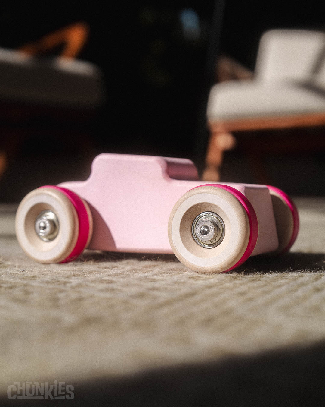 Interior shot of the Chill Pepper Chunkies No04  Wooden Toy Car The Hot Rod Perfectly Pink on a woolen carpet and chairs in the blurry background