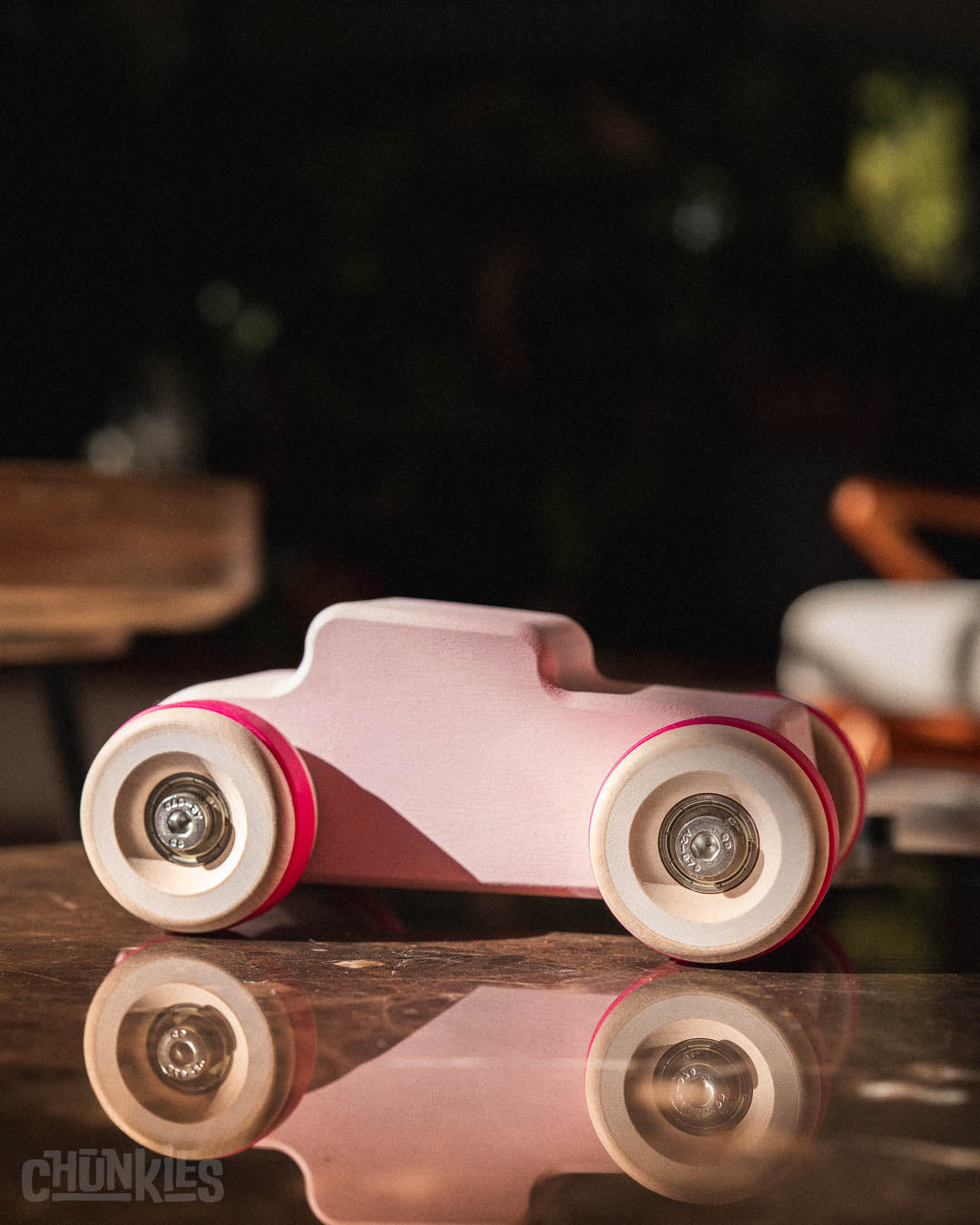 Side view of a Chill Pepper Chunkies No04  Wooden Toy Car The Hot Rod Perfectly Pink on a reflective surface