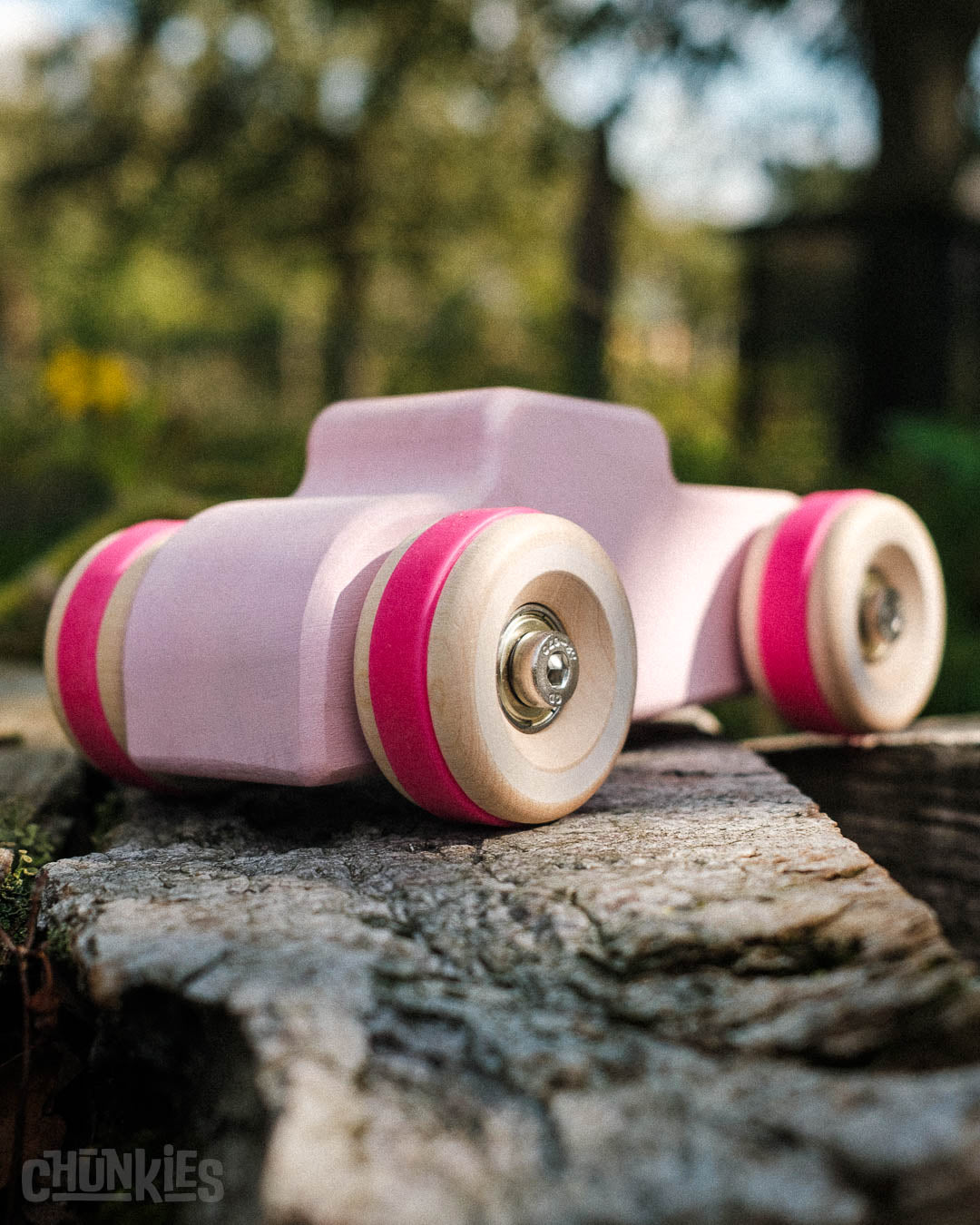 Chill Pepper Chunkies No04  Wooden Toy Car The Hot Rod Perfectly Pink - 3/4 back view outdoor on wooden beams and trees in the background. Certified for safe play for children of 18 months and up