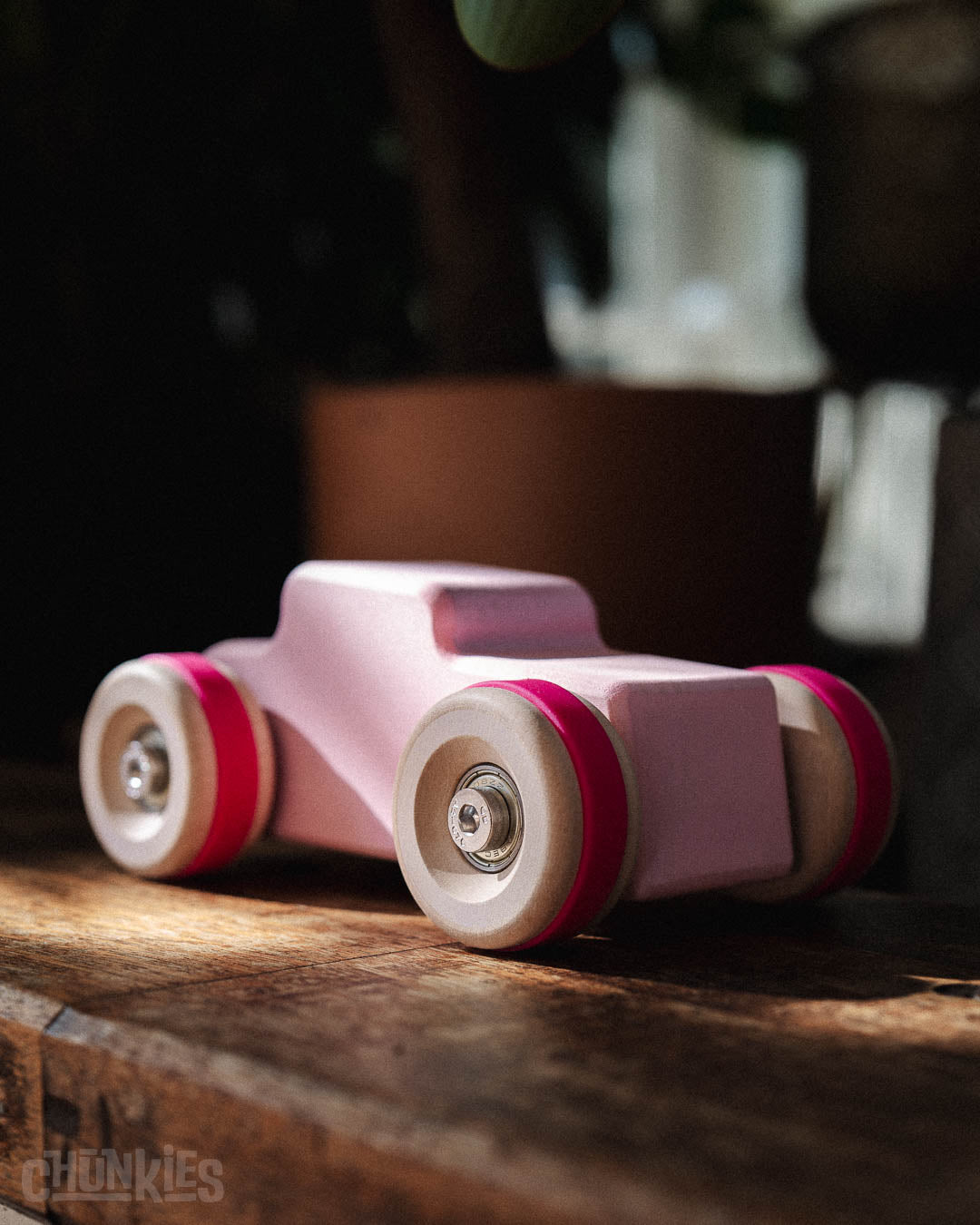 Chill Pepper Chunkies No04  Wooden Toy Car The Hot Rod Perfectly Pink 3/4 front view on a wooden plank in a rustig interior. Made in Europe. Sustainable open ended play, durable with solid wood and real skate bearings.