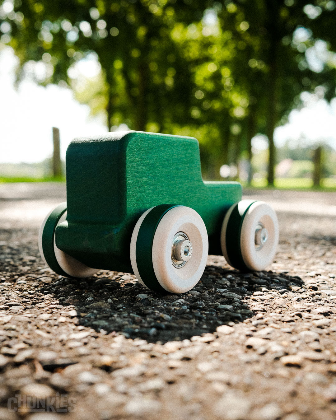 Green toy truck (Chunkies The Explorer) on a gravel surface with trees in the background, Made in Europe ready to travel anywhere