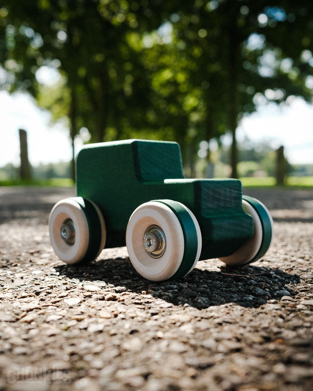 Green toy truck on a gravel surface with trees in the background made by Chill Pepper. This is the Chill Pepper Chunkies No05 Wooden Toy Car The Explorer All-Terrain