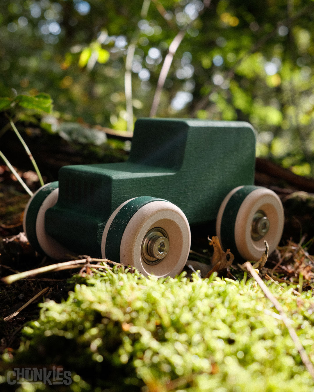 Chill Pepper Chunkies No05 Wooden Toy Car The Explorer All-Terrain in the forest with moss in the foreground and trees in the background. Suitable, since the car is made from sustainably sourced maple wood from Europe and is finished with planet friendly colors