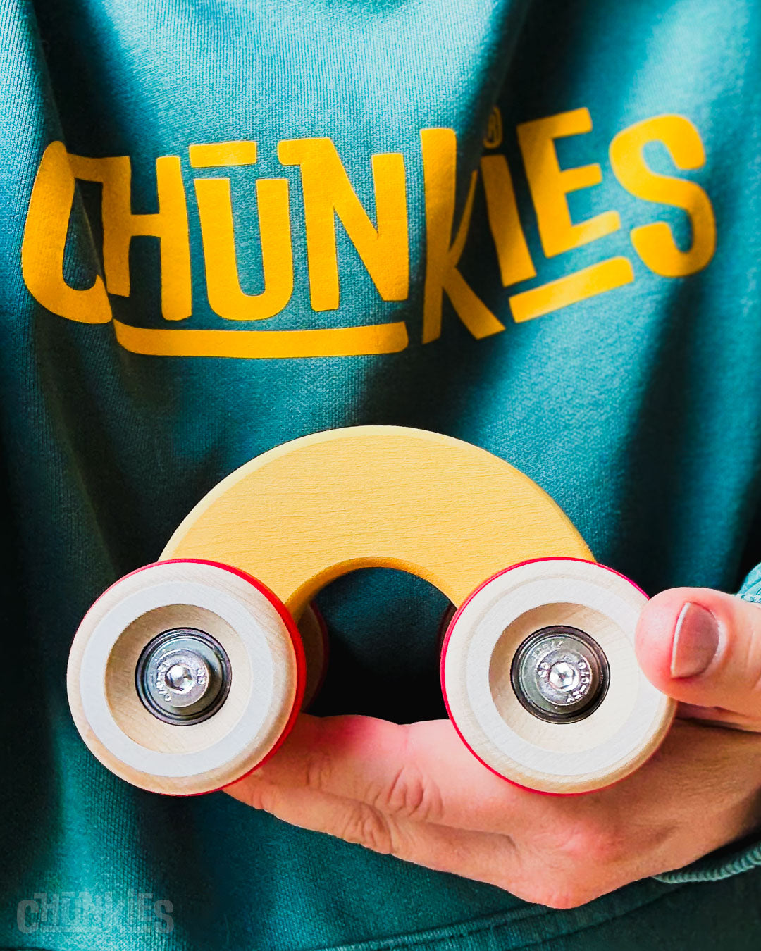 Hand holding the Chill Pepper Chunkies No06 Wooden Toy Car The Rainbow in Yummy Yellow to show scale. The curved silhouet and rounded edges make it perfect to hold by smaller children. The smalles of t he Chunkies collection, but no slouch. Push and tumble: its big wheels and real skate bearings make it ready for any adventure.