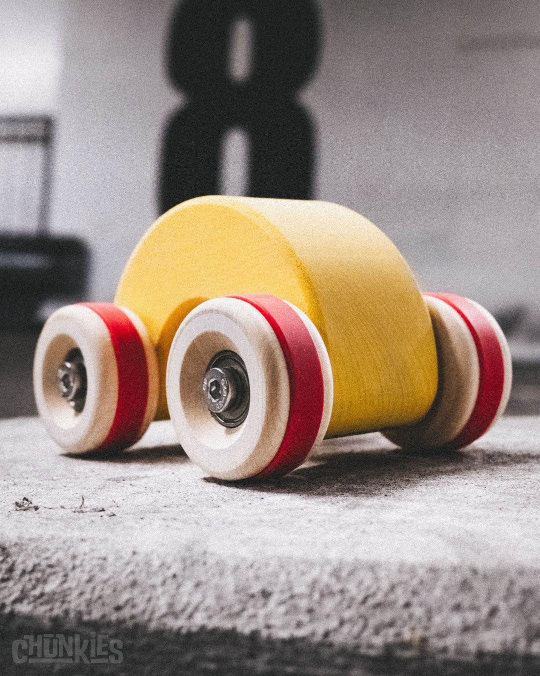 3/4 view of the Chill Pepper Chunkies No06 Wooden Toy Car The Rainbow in a parking garage