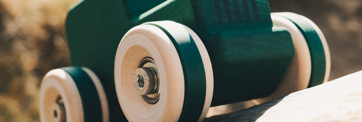 Close-up of a wooden toy car called the Chunkies All-Terrain made by Chill Pepper with green body and big wooden wheels on a blurred natural background