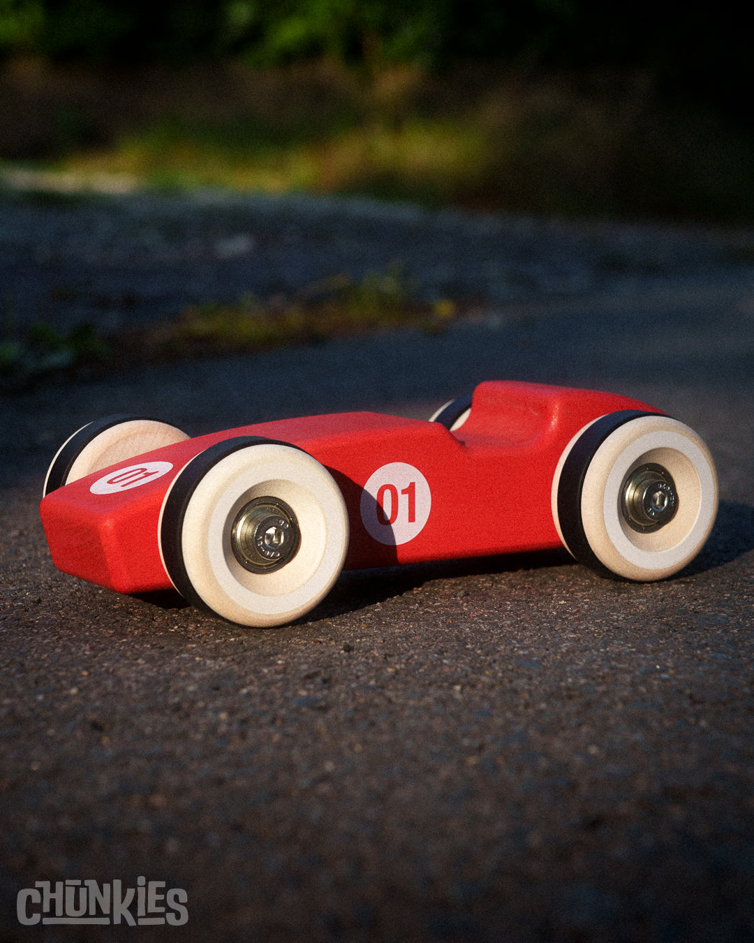 Red toy race car with '01' on a road, brand 'Chunkies' visible. It's big maple wheels and solid wooden body are made in Germany. Hand finished and assembled in The Netherlands. Dutch Design 