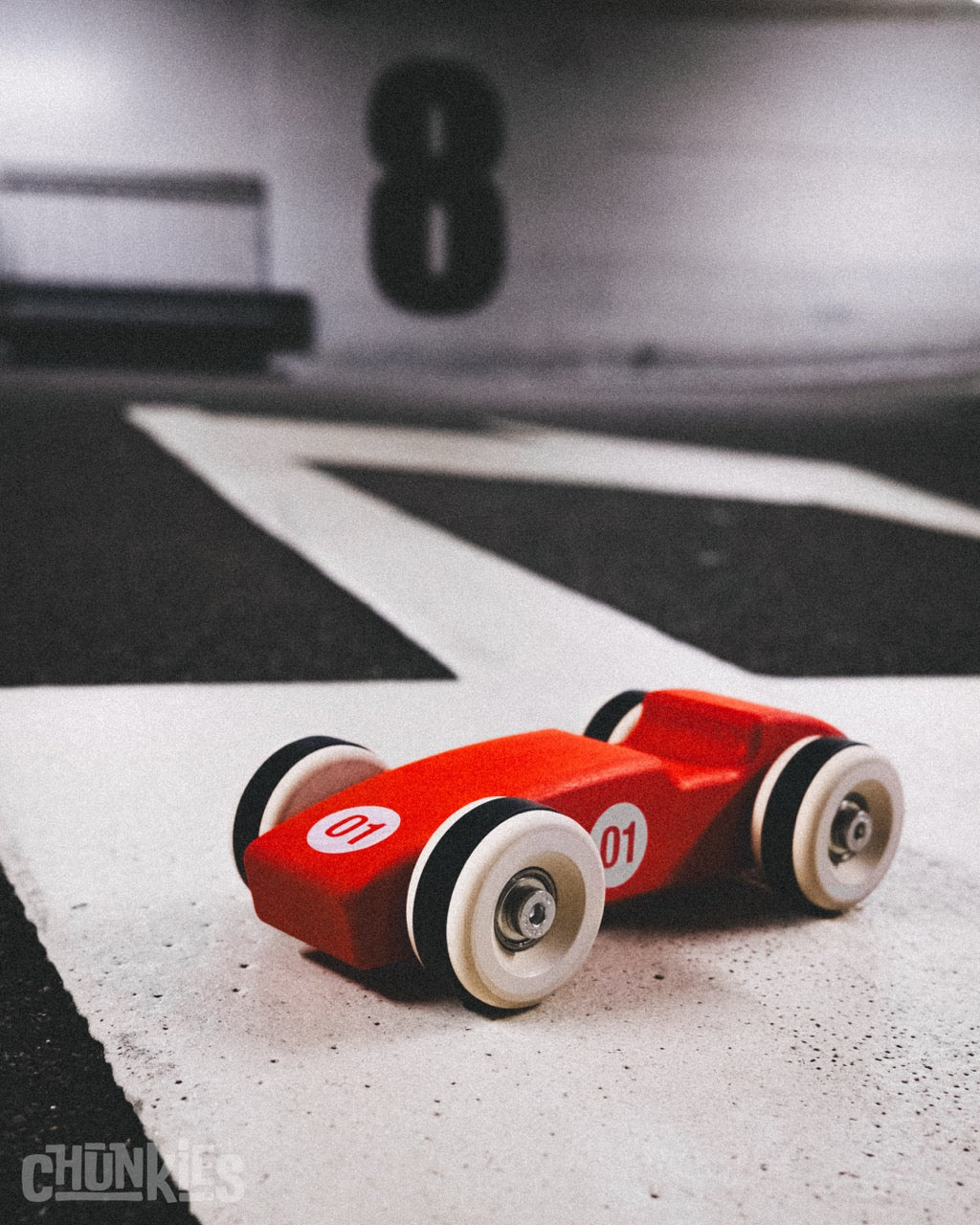 Big red wooden racing toy car with big wooden wheels and black white wall tires. Chunkies classic cigar shaped racer in e parking garage. Made in Europe. Sustainable and child friendly and planet friendly