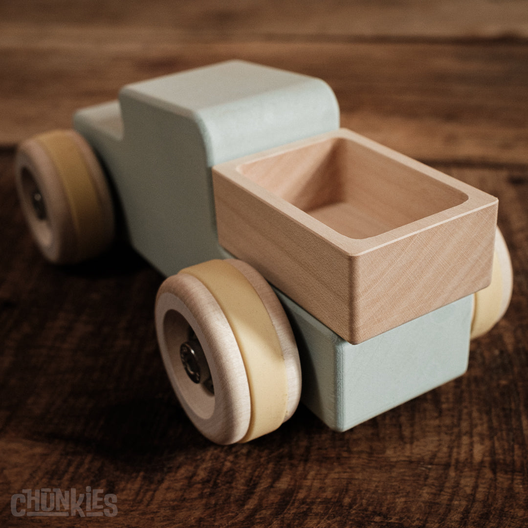Chunkies wooden toy truck with a light blue body and light wooden wheels on a wooden surface. A better view of the load bed and big wooden wheels. Each car comes with two colors of tires so you can customize it