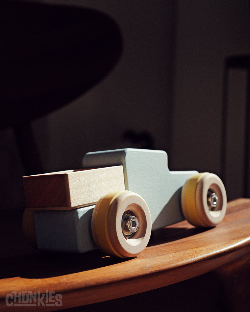 Wooden toy truck called the Chunkies Pick-Up shown on a hand crafted wooden chair and a dark blurry background. Ready for whatever adventure the imagination can come up with.