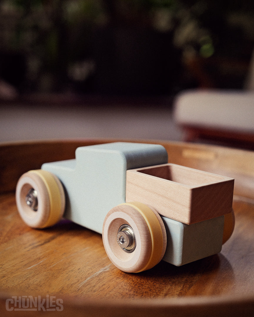 Wooden toy truck made by Chill Pepper with a light blue body and wooden bed on a wooden surface. Model no. 02 The Pick-Up Truck "The Workhorse"