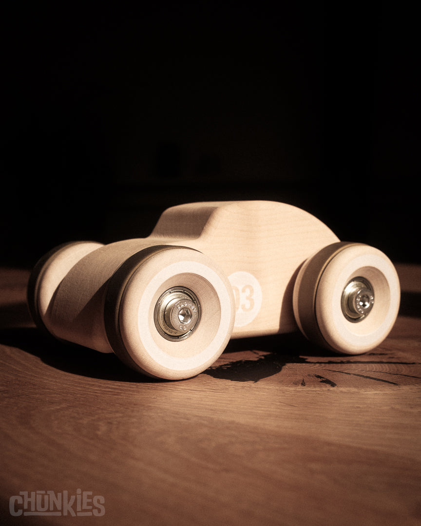 Chunkies: Natural wooden toy car in the shape of a vintage beetle car with wooden wheels, skate bearings and stainless steel hardware. Here shown on a wooden kitchen table with a dark background. Built to last generations. 