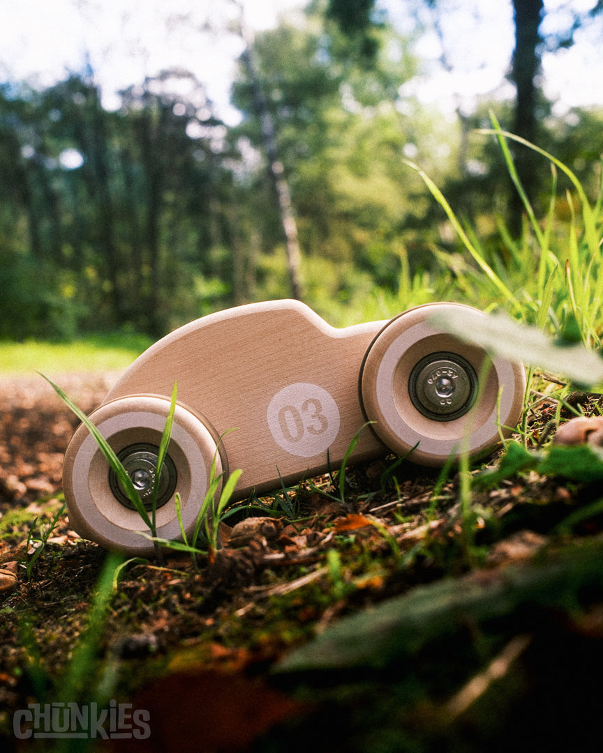 Chunkies No. 03 – Wooden Toy Car The Bug Natural in the grass with a forest in the background. This big wooden toy car is in the shape of a vintage beetle car. Made from European sustainable maple wood. Big wooden tires and real skate bearings offer a superb ride.